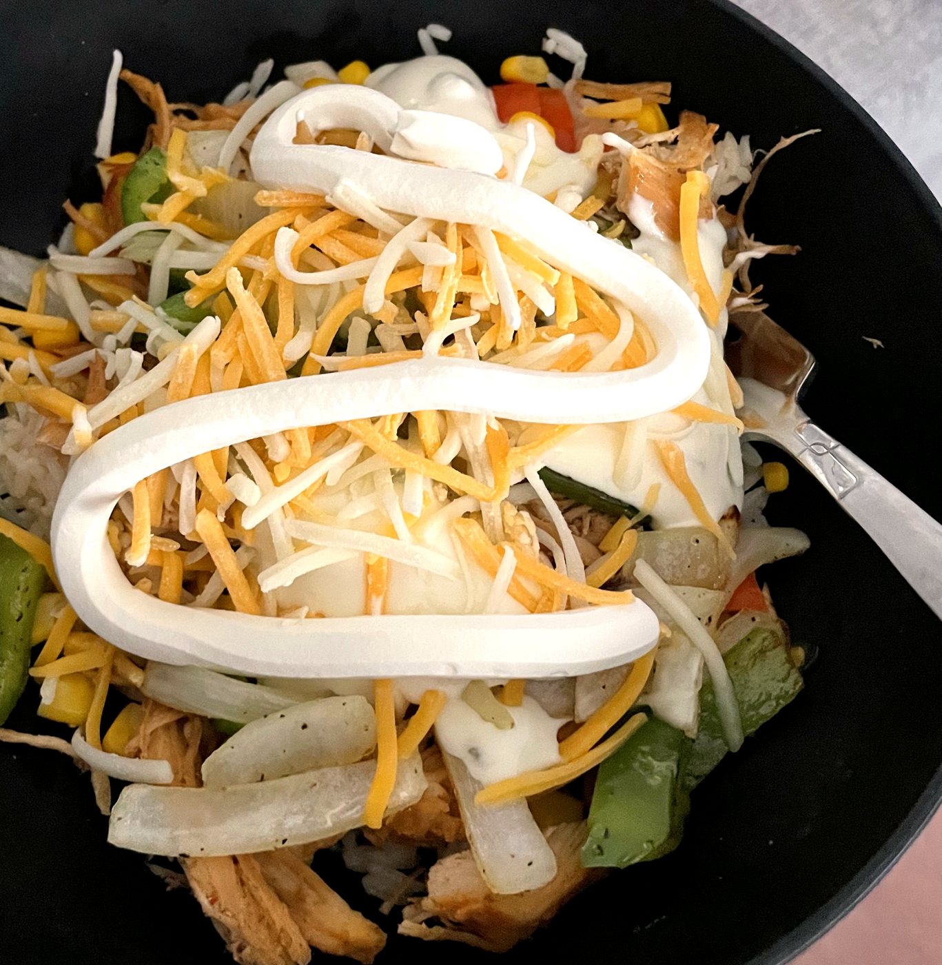 A homemade burrito bowl with chicken, peppers, onions, corn, cheese and sour cream