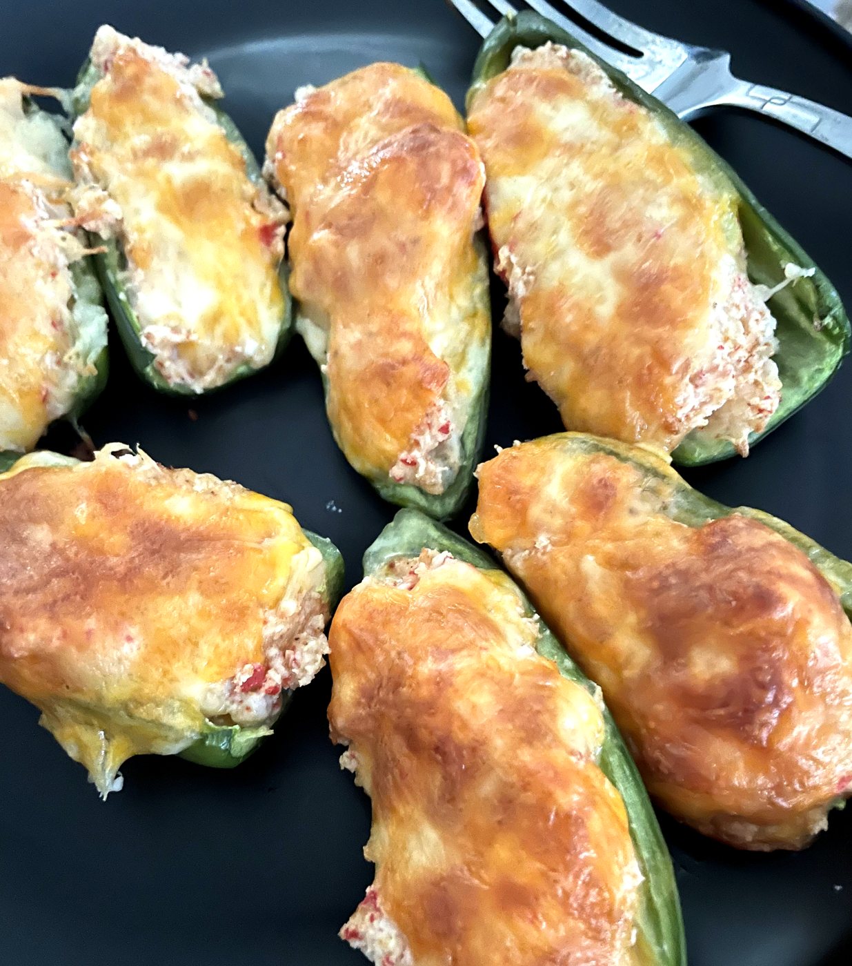 Crab stuffed jalapeño poppers with browned melted cheddar on a black plate