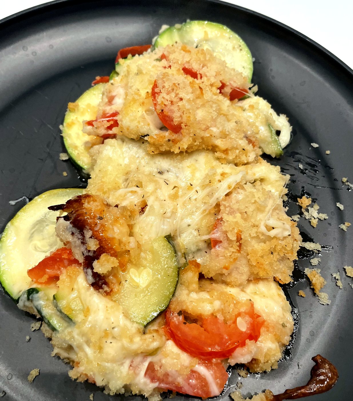 A serving of zucchini tomato bake with golden panko and melted cheese on a black plate